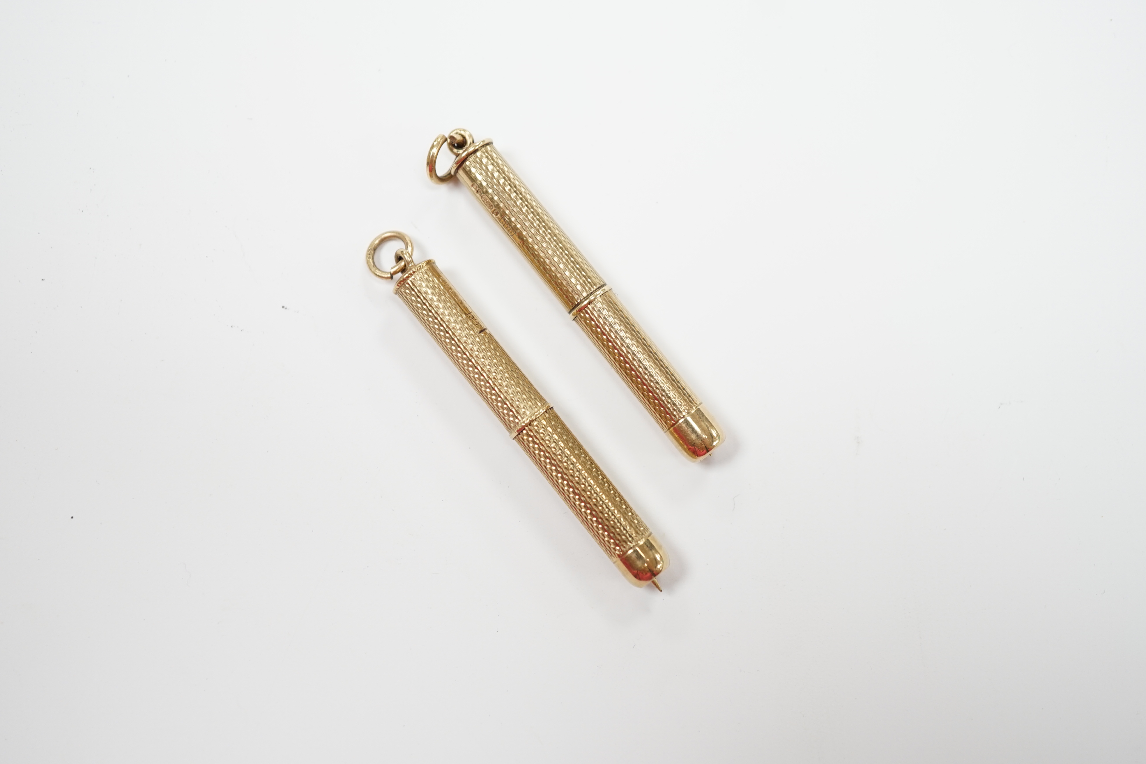 Two engine turned 9ct gold cased propelling toothpicks, 43mm.